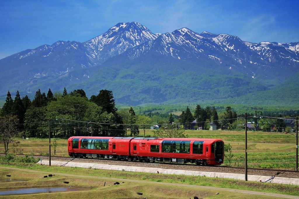 A beautiful train in a beautiful setting. The body of the train is colored vermilion to offer a warm contrast with the surrounding natural scenery
